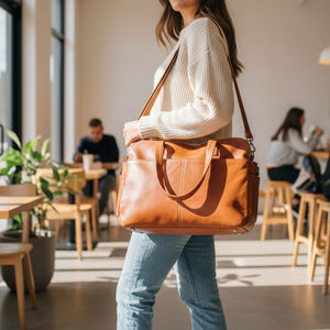 Brown leather bag held by a person with a neutral background